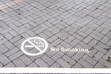 Symbol white paint on floor NO SMOKING on ground walkway brick.  NO SMOKING Image of cigarette in white circle. Symbol that must respected prohibition in public areas. Sign warning on floor footpath.