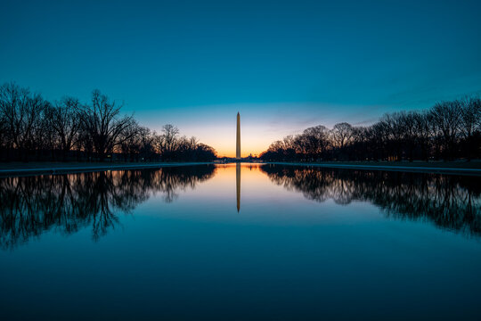 View of the Washington Monument piercing the tranquil dawn sky, its reflection shimmering in the still waters of the reflecting pool, Washington, D.C., United States.