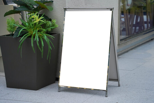 Blank white outdoor advertising stand sandwich board mock up template. Clear street signage board placed by an outdoor dinning area of a restaurant.