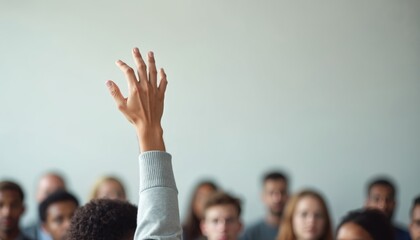 Person raises hand in crowded room. Audience listens in background. Hand raised to ask question participate. People gathered in meeting seminar setting. Individual engaged, interactive.