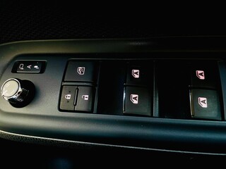 A close-up view of a vehicle's driver-side control panel, featuring power window switches, door lock/unlock buttons, a window lock button, and a knob for adjusting the side mirrors.