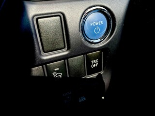 A close-up of a vehicle's lower dashboard panel featuring the blue illuminated "POWER" start/stop button, along with buttons for various functions like TRC OFF (Traction Control) and controls for the 