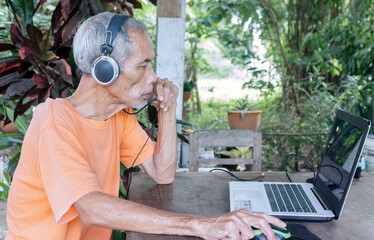 Senior man focused on laptop in garden setting, wearing headphones. Blending technology with tranquil outdoor life.