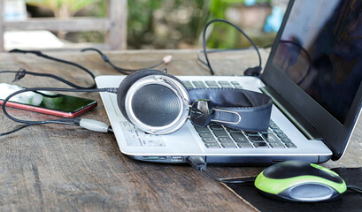Close-up of black and silver over-ear headphones resting on a laptop keyboard and screen on a rustic wooden table, with a smartphone nearby.