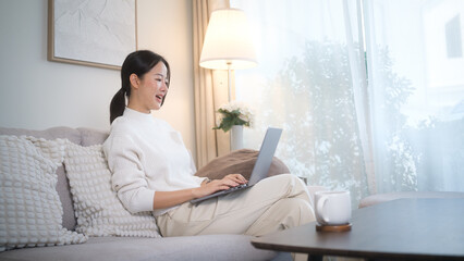 Fototapeta premium Woman on a video call using her laptop in a bright and cozy living room.