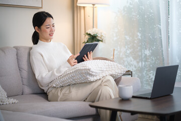 Fototapeta premium Smiling woman relaxing on sofa while using digital tablet in cozy living room.