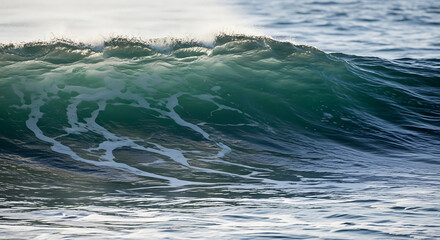 A close up shot of a wave crashing with white foam and blue green water in the ocean on a sunny day