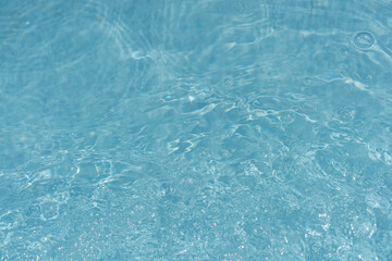Blue water with ripples on the surface. Defocus blurred transparent blue colored clear calm water surface texture with splashes and bubbles. Water waves with shining pattern texture background.