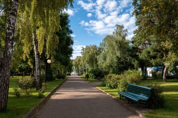 Brick path through a green park with trees and a blue bench under a partly cloudy sky