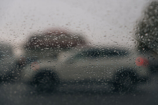 From inside a car during heavy rain. Focus is on the water droplets running down the glass. The blurred silhouettes of cars are visible through the curtain of water, depicting movement in bad weather.