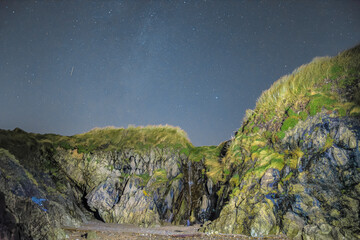 Starry night over rugged Irish cliffs with cascading water and moss-covered rocks in a secluded...