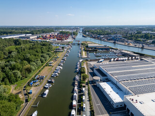 Obraz premium Klein-Willebroek, Willebroek, Antwerp, Belgium, 13th of May, 2025, A stunning aerial shot of a canal with vibrant boats, large warehouses, and lush greenery all around