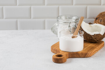 Creamy coconut yogurt on wooden board with half coconut and jar in kitchen setting. Copy space