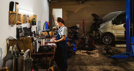Female worker using laptop in local auto repair shop.