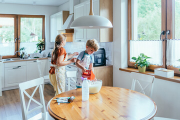 Close up of child hands using orange hand mixer to blend pancake batter in bowl
