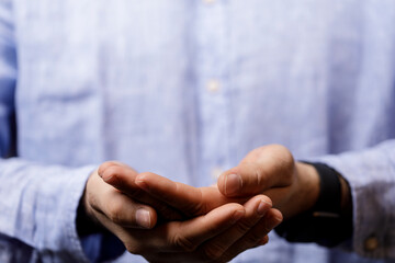 Fototapeta premium Close-up of a man's hands held open, palms up, against a soft blue shirt backdrop. The image conveys giving, receiving, or anticipation.