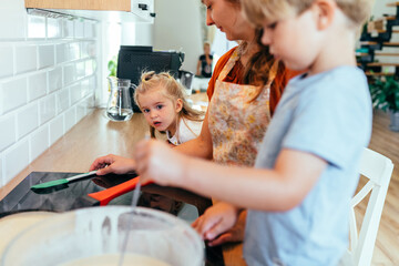 Mother cooking with son and daughter in bright family kitchen