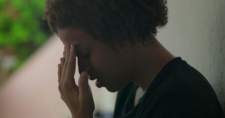 Young boy in emotional distress, hands covering face, crying, standing against wall, African descent, outdoor setting, close-up