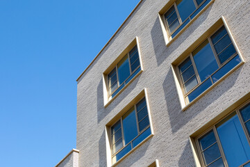 Gray brick building corner with large windows under clear blue sky. Architectural detail for residential or commercial property visuals. Real photo