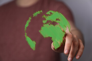 A person's hand interacts with a vibrant green digital globe, symbolizing environmental care,...