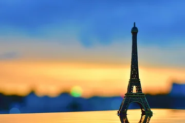 Fotobehang Eiffeltoren A miniature Eiffel Tower stands gracefully against a vibrant sunset sky, symbolizing dreams of travel and the charm of Parisian evenings. Chasing Paris dreams under golden skies.  © RK