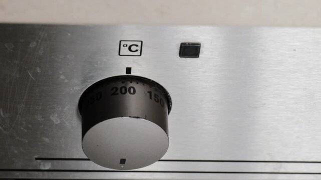 Hand turning oven dial to set desired cooking temperature, close-up of control panel marked in degrees Celsius