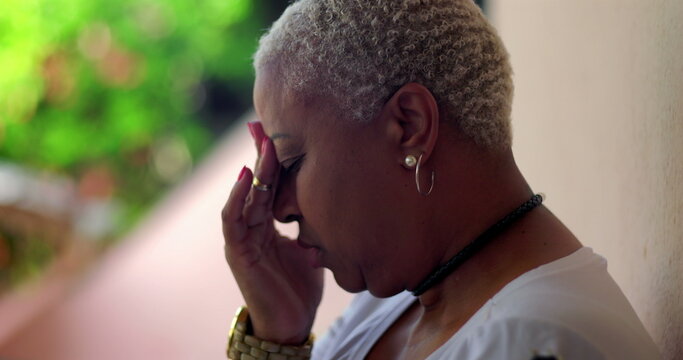 Hispanic Latina of African descent woman sitting outdoors, hand on forehead, showing deep thought, feeling overwhelmed and regret during difficult times, natural background