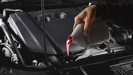 Mechanic hand pouring red transmission fluid into car engine under hood close up. Concept of auto repair, lubricant technology, and professional service visuals for technical communication.