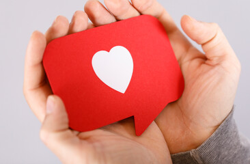 Obraz premium Close-up shot of hands gently holding a red heart-shaped speech bubble. Represents love, affection, support, and social interaction. Ideal for V