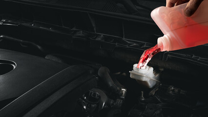 Mechanic hand pouring red coolant fluid into car reservoir close-up under hood. Concept of car care, temperature regulation, and automotive cooling system maintenance visuals.