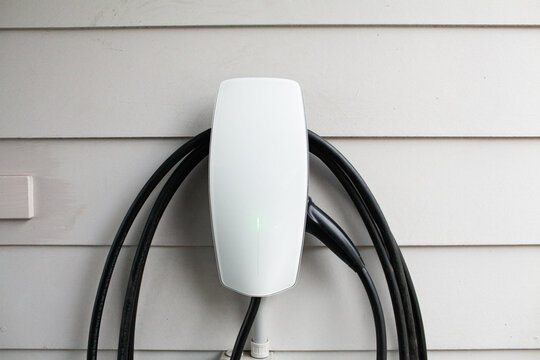 EV car charger plug and cable on side of white weatherboard home