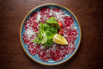 A plate of beef carpaccio topped with parmesan, greens, and lemon, exemplifying gourmet dining
