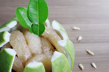 Pomelo flesh is arranged in the peel, decorated with fresh green leaves, on a wide wooden table.

