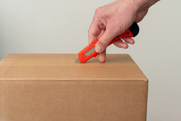 Hand with red and black box cutter is opening a box. White space.