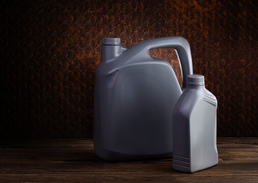 A set of oil gallons, lubricant drums, or motor oil bottles, placed on a table against a rusty old iron background. - Powered by Adobe
