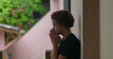 One Hispanic young boy of African descent with curly hair, eyes closed, hands clasped in prayer,...