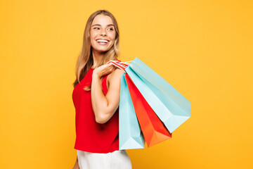 Side view young smiling woman wear red casual clothes hold in hand paper package bags after...