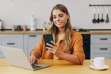 Young happy housewife IT woman wear orange shirt casual clothes hold use work on laptop pc computer...
