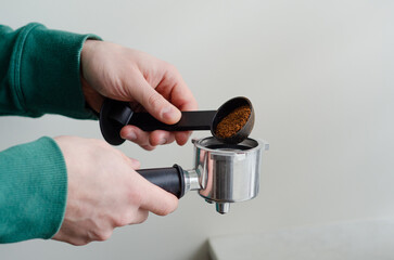 Cozy morning with mans hands scooping ground coffee into portafilter coffee machine
