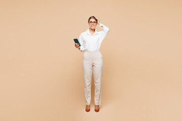 Full body young shocked sad scared employee business woman corporate lawyer wear classic formal white shirt work in office hold in hand use mobile cell phone isolated on plain beige background studio