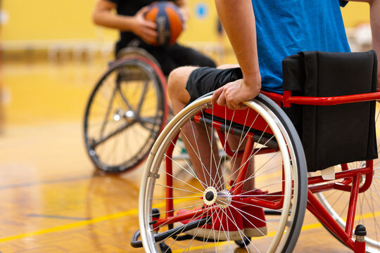 two wheelchairs support players on a basketball court and one player is holding a basketball