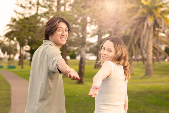 happy couple posing in the park with hands reaching back to camera