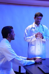 group of doctors is having a treatment planning meeting and a handsome Caucasian male doctor presents at the front of the room, discussing research data with slides on the wall.