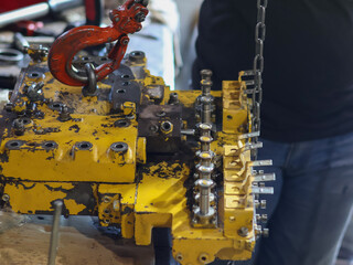 Close-up of a worker's hands using a heavy-duty orange lifting hook and chain to move or position a control valve transmission in a workshop.