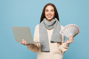 Young IT woman wears pink sweater scarf work hold money cash use laptop pc computer isolated on plain blue background studio portrait. Healthy lifestyle ill sick disease treatment cold season concept.