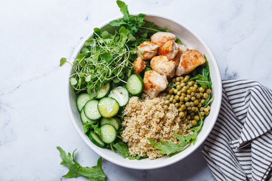 Balanced quinoa, arugula, chicken, cucumber and pea lunch bowl.