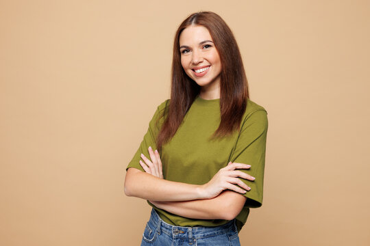 Fototapeta Side view young smiling happy woman wears olive green t-shirt casual clothes hold hands crossed folded look camera isolated on plain pastel light beige background studio portrait. Lifestyle concept.