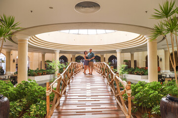 Loving adults stand hugging decorative bridge inside a building.