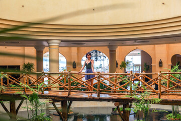 A pretty female tourist in light clothing stands on decorative bridge inside a hotel.