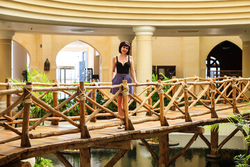 A pretty female tourist in light clothing stands on a decorative bridge inside a hotel.
